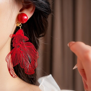 Détail de clip d'oreille poisson rouge évidé avec perle rouge porté par un mannequin
