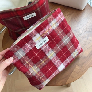 Vue détaillée d'une trousse de maquillage en tweed à carreaux rouges sur table en bois