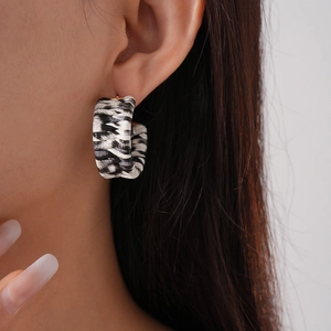 Detail of a C-shaped earring with black and white woven texture and golden base