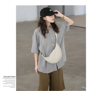 Detail shot of a beige nylon crescent crossbody bag styled with a plaid shirt and brown pants