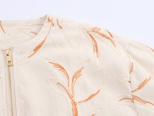 Detailed close-up of beige linen texture with orange leaf embroidery and metal zipper
