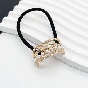 Close-up of black elastic hair tie featuring gold metal twist band and white pearls