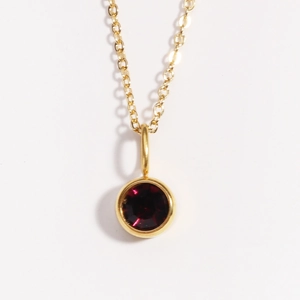 Detail of a gold birthstone necklace featuring a round red crystal pendant on a thin chain
