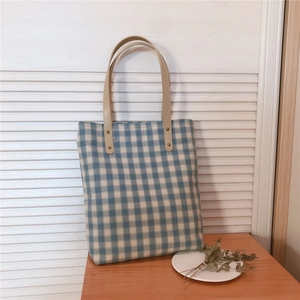 Close-up of blue gingham canvas tote bag with brown leather handles and gold metal rivets