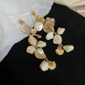 Detailed view of long shell tassel earrings with gold irregular shell charms on black velvet