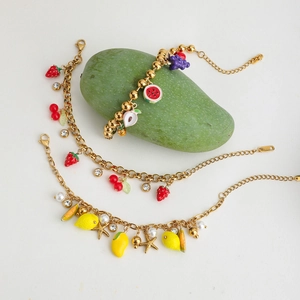 Detailed shot of gold charm bracelets with colorful summer fruit pendants and pearls