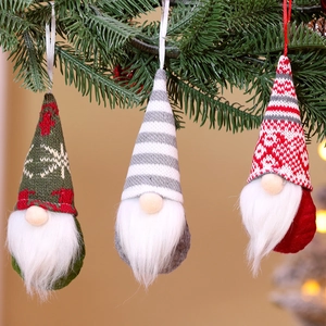 Close-up of three knitted Christmas gnomes hanging on green pine branches for tree decor