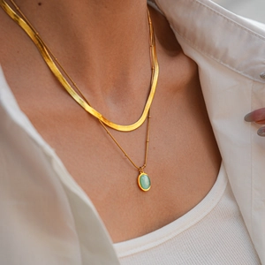 Détail d'un collier doré double couche avec chaîne serpent et pendentif opale verte