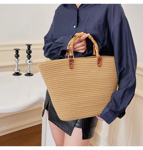 Detail of a large straw woven tote bag featuring natural bamboo handles and rivets