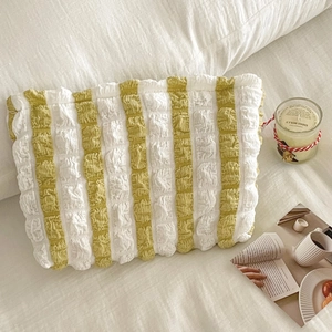 Portable yellow and white striped bubble puff cosmetic bag on cozy white bedding