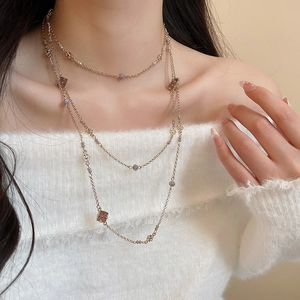 Close-up of layered gold chain necklace with grey beads and brown clover pendants on a model