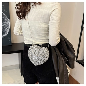 Detailed view of silver heart-shaped evening clutch bag with sparkling rhinestones on model