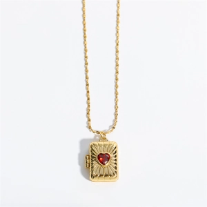 Vintage gold locket necklace with sunburst texture and red heart zircon on white background