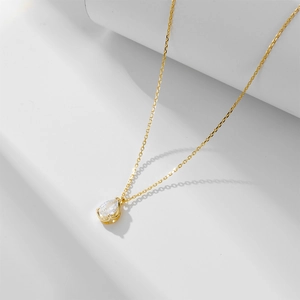 Detail of a minimalist gold teardrop zircon pendant necklace on white geometric steps