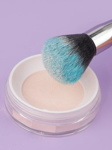 Close-up of a blue gradient powder brush picking up fine makeup powder from a jar