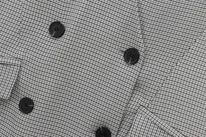 Macro shot of grey houndstooth fabric texture with a black round button on a dress