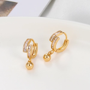 Detail of gold hoop earrings with zircon baguette stones and polished metal ball pendants