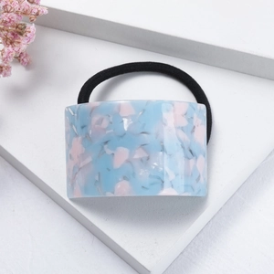 Close-up of marble pattern acetate hair tie in blue and pink on white display stand