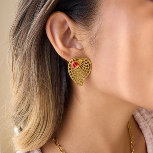 Gold hollow heart earrings with red ladybug detail worn by a model in a close-up shot