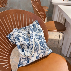 Detailed texture of blue botanical print on white canvas tote bag placed on a wooden chair