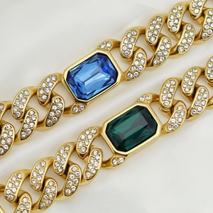 Dettaglio di bracciali a catena cubana dorati con grandi gemme rettangolari blu e verdi