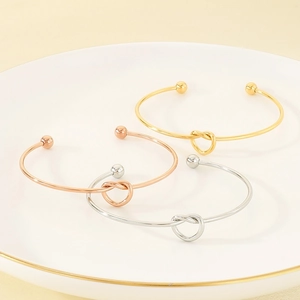 Detailed view of knot-style open cuffs in gold, silver, and rose gold on a ceramic tray