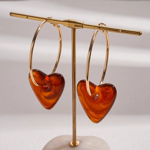 Detail of amber acrylic heart pendant on a gold hoop earring hanging on a stand
