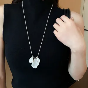 Minimalist silver chain necklace with three white petal pendants on a black top model