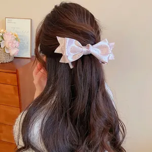 Elegant pink satin bow hair clip with black polka dots on brunette wavy hair