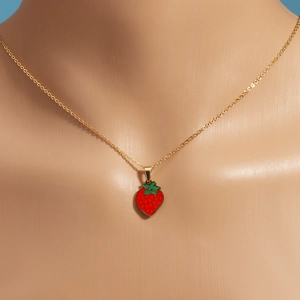 Close-up of a gold necklace featuring a red enamel strawberry pendant on a mannequin