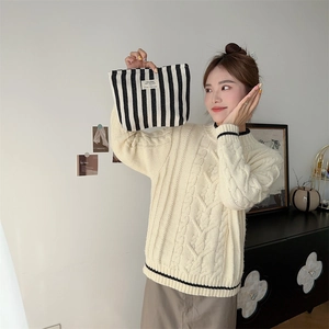 Close-up of black and white striped canvas toiletry bag held by a model at home