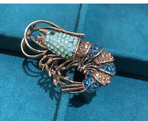 Macro view of crystal-encrusted lobster brooch showing blue rhinestones and gold plating