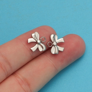 Close-up of silver steel bow-knot jewelry charms held between fingers on blue background
