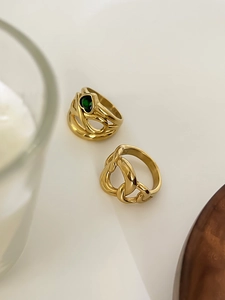 Close-up of golden intertwined rings featuring a green heart-shaped gemstone detail
