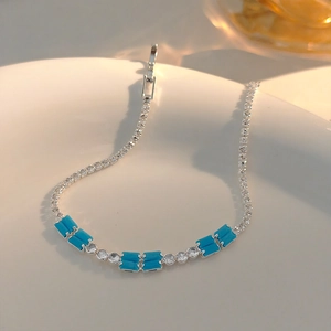 Close-up of silver chain bracelet with sky blue rectangular gems and round zircons on ceramic