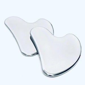 Macro shot of two heart-shaped stainless steel Gua Sha tools on a clean white background