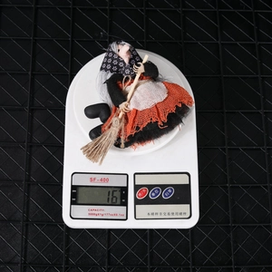 Detail showing a miniature Halloween witch doll in a purple dress on a digital scale