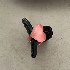 Detail of a black plastic hair claw clip with a 3D pink heart on a grey surface
