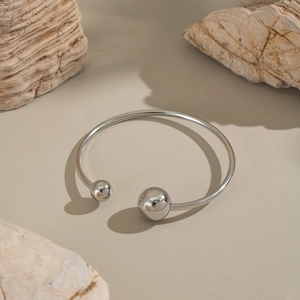 Macro shot of polished silver stainless steel open bangle with asymmetrical ball finials