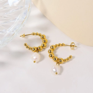 Detail view of gold beaded C-shape earrings with elegant white baroque pearl pendants