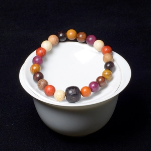 Macro detail of multicolored wooden beads bracelet resting on a white ceramic tea bowl