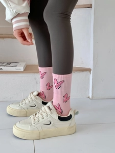 Detail view of pink crew socks with heart patterns paired with beige sneakers and leggings