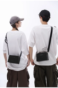 Detail of couple wearing black textured box cross-body bags with CONE KNOWN embossed text