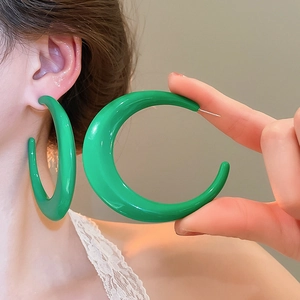 Close-up of chunky bright green C-shape earrings with a glossy ceramic glaze finish