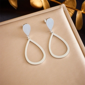 Macro shot of silver teardrop earrings on golden velvet jewelry box with dried flowers