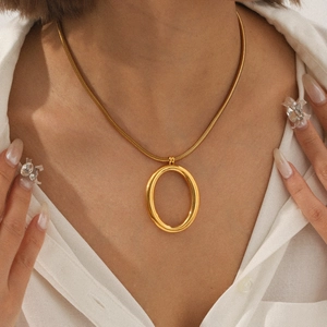 Close-up of gold snake chain necklace with oval pendant worn on a white shirt
