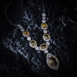 Detailed view of yellow oval gemstone necklace with silver chain on black rock