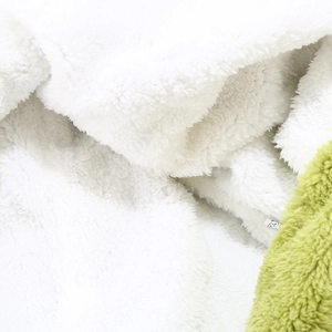 Detail of plush dinosaur hat fabric showing green and white faux fur with care label