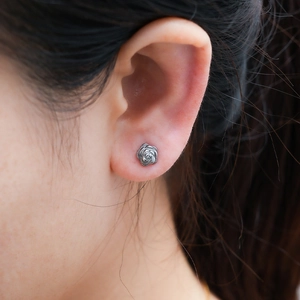 Detailed close-up of a silver-toned steel rose stud earring worn on a model's ear