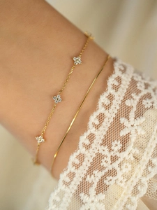 Detail of layered S925 silver 18K gold clover bracelets with zircons on a female wrist